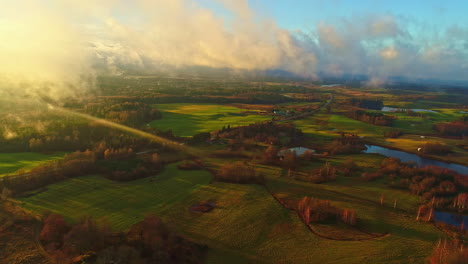 Sunset-over-a-lush-valley-with-a-river,-dramatic-clouds-casting-shadows-on-the-landscape,-aerial-view