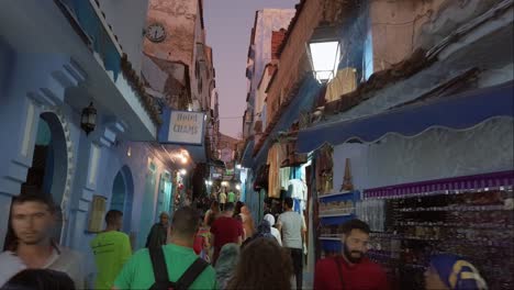 Sightseeing-tourists-walking-through-the-narrow-pedestrian-streets-surrounded-by-souvenir-shops-in-the-old-blue-town-center-of-Chefchaouen,-Morocco