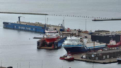 The-large-blue-ship-is-moored-at-the-quay,-the-large-red-ship-is-dry-docked,-and-behind-it-is-an-empty-dry-dock-in-Frederikshavn-Orskov-Shipyard,-Denmark