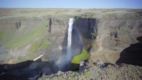 A-steep-waterfall-surrounded-by-rocky-cliffs-in-Iceland-creates-a-small-rainbow---Slow-motion