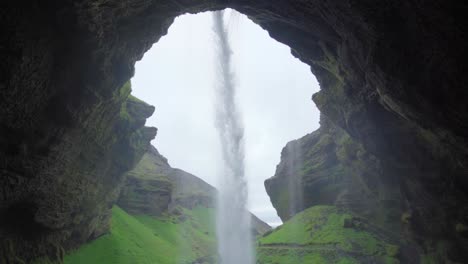 A-view-from-behind-a-waterfall-in-Iceland,-looking-out-at-the-canyon-beyond---Slow-motion