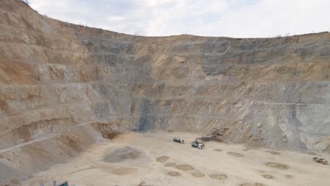 Drone-shot-rising-in-front-a-large-quarry-site-with-machines-at-work,-cloudy-day