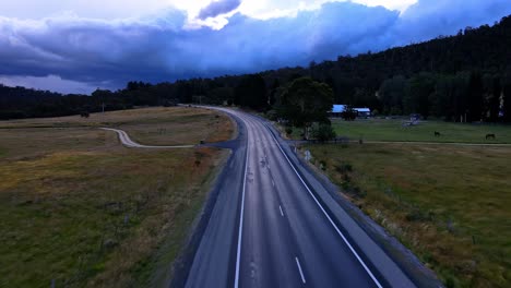 Drone-shot-of-rural-alpine-highway-road-with-dark-and-dramatic-storm-clouds-on-the-horizon-in-Crackenback,-NSW,-Australia