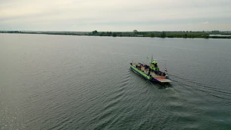 Ferry-sails-in-the-middle-of-the-river-drone-flies-behind-the-ferry,-flag-at-half-mast-in-connection-with-Remembrance-Day