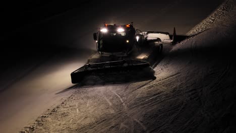 Snow-groomer-PistenBully-working-at-night-in-the-Dolomites,-Italy,-lights-on-and-grooming-the-slopes