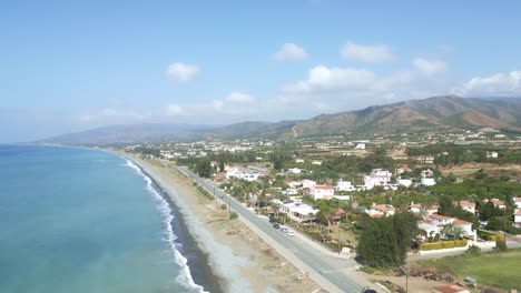 Bahía-De-Chrysochous-En-Chipre,-Mostrando-Una-Serena-Playa-Y-Exuberantes-Colinas-Bajo-Un-Cielo-Azul,-Vista-Aérea