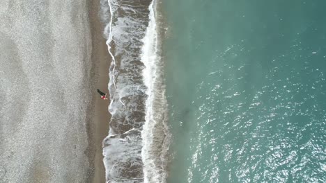 A-lone-person-walking-on-pissouri-beach-in-cyprus,-waves-gently-crashing,-aerial-view