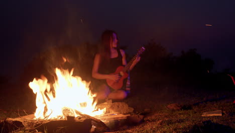 Asiatische-Frau-Spielt-Ukulele-Gitarre-Vor-Dem-Feuer-Bei-Nacht-Outdoor-Camping