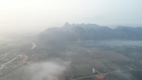 drone-shot-of-foggy-misty-morning-in-Vang-Vieng,-the-adventure-capital-of-Laos