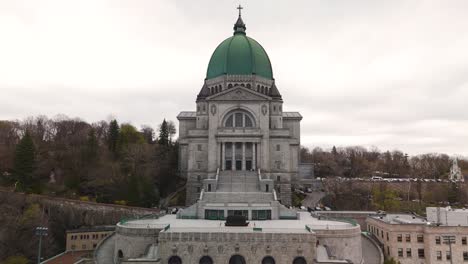 Vista-Aérea-Frontal-Del-Oratorio-De-San-José-Del-Monte-Real,-Montreal,-Drone-Acercándose-A-La-Antigua-Basílica-Católica-Romana-Cúpula-Verde-Que-Revela-Un-Impresionante-Paisaje-Urbano-A-Distancia-Durante