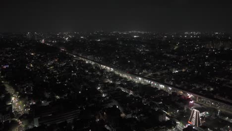 Toma-Aérea-Nocturna-De-Drones-De-La-Vía-Del-Metro-Pasando-Por-El-Tráfico-En-La-Autopista