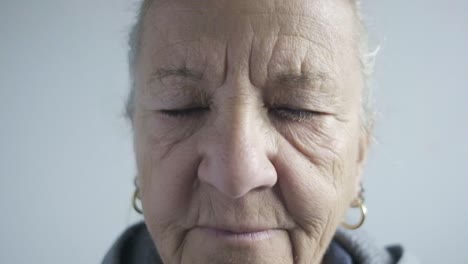 Ältere-Kaukasische-Dame-Schaut-In-Die-Kamera,-Falten,-Nahaufnahme,-Blinkende-Blaue-Augen,-Weißes-Haar,-Ohrringe-Und-Sportbekleidung,-Gesichtsporträt