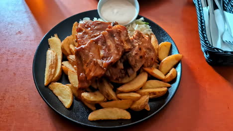 Dolly-forward-view-of-food-in-black-plate,-cooked-ribs-with-wedge-potatoes-aside