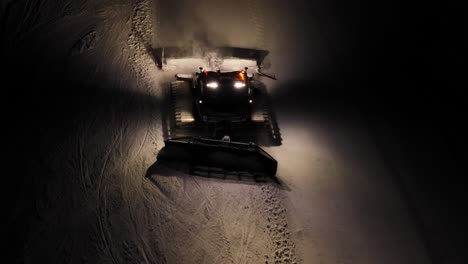 Snow-groomer-working-at-night-in-the-Dolomites,-Alpine-glow-on-snow,-high-angle-view