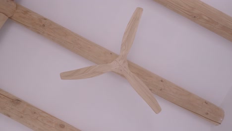light-wood-fan-seen-from-below,-on-a-light-wood-beam-on-a-white-ceiling