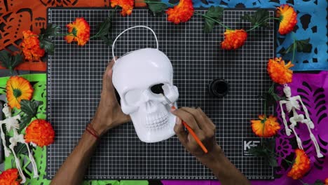 Hands-painting-white-skull-with-vibrant-flowers-for-Day-of-the-Dead,-top-view,-crafting-concept