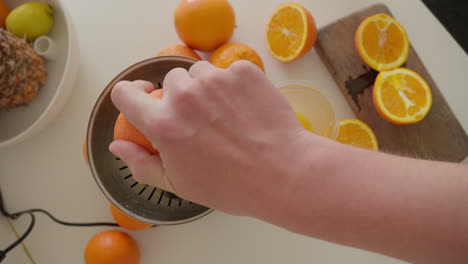 Fresh-orange-juice-being-squeezed-by-hand-in-home-kitchen-with-electric-juicer