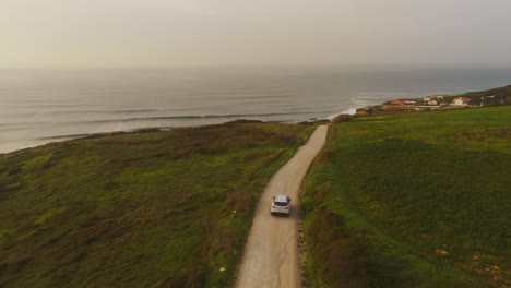 Aerial-view-of-a-modern-SUV-driving-on-the-Magoito-coast,-sunset-in-Portugal