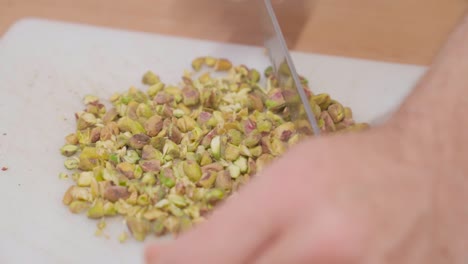 Chef-finely-chopping-green-pistachios-on-a-white-cutting-board-in-slow-motion,-close-up