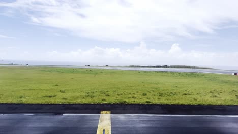 An-empty-runway-after-rain-with-lush-green-fields-and-cloudy-skies,-wet-tarmac,-aerial-view