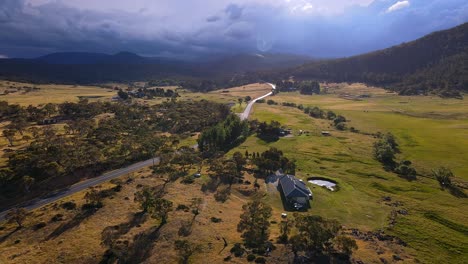 Rural-farm-house-and-highway-near-Kosciuszko-National-Park-with-storm-clouds-and-sun-rays,-Crackenback,-NSW,-Australia
