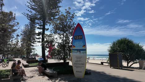 People-chilling-on-an-esplanade-near-a-beach-around-a-surf-board-clock