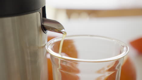 Orange-juice-pouring-into-clear-glass-cup-from-electric-juicer