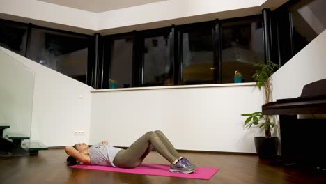 Woman-doing-crunches-on-a-pink-yoga-mat-in-a-home-interior-at-night,-low-angle-view