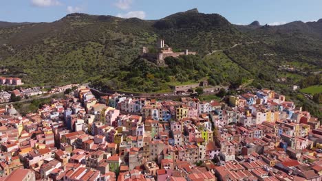 Drone-footage-showcases-the-enchanting-town-of-Bosa,-Sardinia,-with-its-surrounding-forest-and-historic-castle,-a-captivating-perspective-for-stock-footage