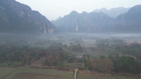 drone-shot-of-road-into-the-misty-valley-in-Vang-Vieng,-the-adventure-capital-of-Laos