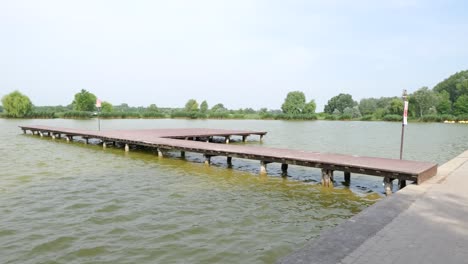 Panning-view-of-wooden-pier-on-shore-of-lake-in-city-park