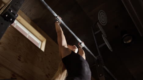 Blonde-female-athlete-in-gym-does-CrossFit-kipping-pull-ups,-upwards-slomo-view