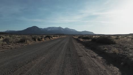 Moving-along-the-roads-of-Utah,-USA,-the-drone-takes-a-low-flight,-gradually-ascending-to-unveil-the-desolate-and-arid-landscapes,-painting-a-captivating-picture-of-the-terrain-below