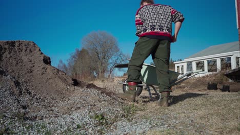 Man-Shoveling-Soil-Into-Wheelbarrow-At-Farm-In-Indre-Fosen,-Norway