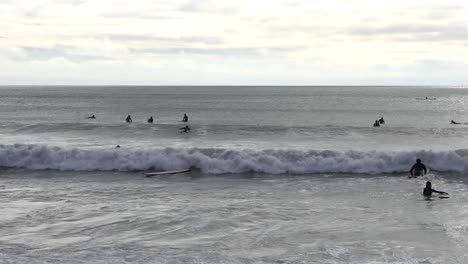 Los-Surfistas-Reman-Y-Empujan-A-Través-De-Las-Olas-Entrantes---Scarborough-Bay,-Christchurch,-Nueva-Zelanda