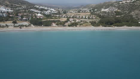 Pissouri-beach-in-cyprus,-with-clear-turquoise-waters-and-coastal-town-backdrop,-aerial-view