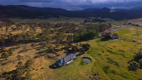 Aerial-tilt-shot-of-rural-farm-house,-country-road-and-storm-clouds-at-Crackenback,-New-South-Wales,-Australia