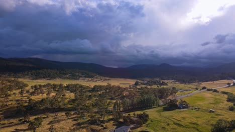 Cinematic-aerial-of-dark-rain-clouds-above-Kosciuszko-National-Park-with-golden-farmland-in-foreground,-Crackenback,-NSW,-Australia