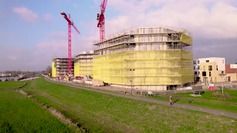 Sonnenuntergangspanorama-Der-Roten-Kräne,-Die-Sich-über-Der-Baustelle-Noorderhaven-Erheben,-Teil-Der-Stadtentwicklung-Und-Des-Wohnviertels,-Gesehen-Von-Den-Auen-Des-Flusses-Ijssel