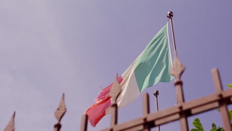 Bandera-Italiana-Ondeando-En-La-Brisa-Contra-Un-Cielo-Azul-Claro,-Vista-En-ángulo-Desde-Abajo