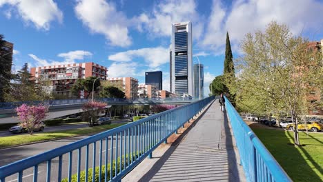 Urban-Scenery-in-Madrid-with-Skyscrapers,-Pedestrian-on-Bridge-and-Cars-during-Spring