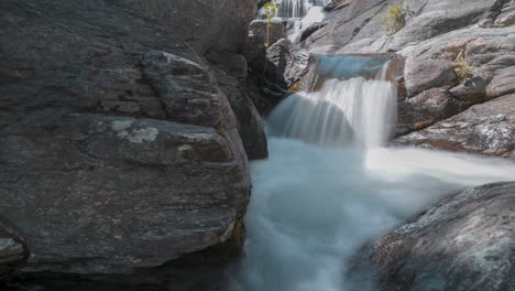 Mountain-stream-cascading-over-rocks,-a-serene-waterfall-in-a-natural-setting,-captured-in-smooth-timelapse
