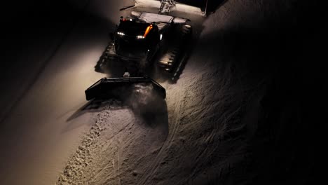 Snow-grooming-machine-at-work-at-night-in-the-Dolomites,-Italian-Alps,-illuminated-by-powerful-lights
