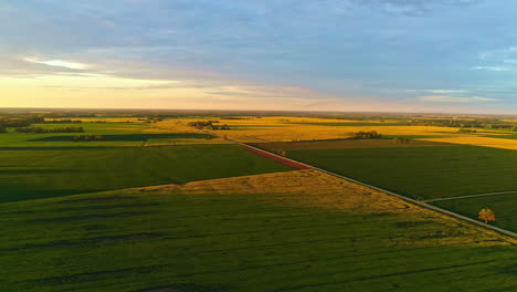 Golden-sunrise-over-tranquil-rural-landscape-with-long-road,-aerial-view