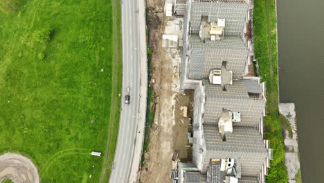 aerial-a-dynamic-construction-site-next-to-a-bustling-road,-contrasted-by-a-stretch-of-green-grass