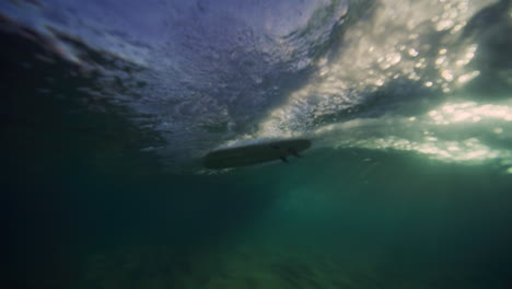 Una-Luz-Brillante-Ilumina-Al-Surfista-Con-Los-Brazos-En-Alto,-Vista-Desde-Debajo-De-La-Superficie-Del-Agua-Clara