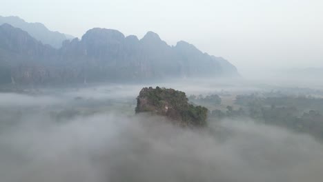 drone-shot-of-cliffs-through-the-fog-in-Vang-Vieng,-the-adventure-capital-of-Laos