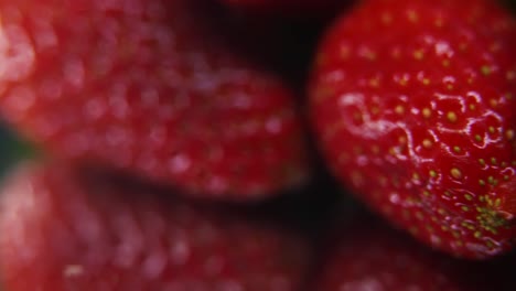 Macro-detailed-video-of-a-pile-of-strawberries,-red-strawberry,-green-leaf,-tiny-yellow-seeds,-on-a-rotating-reflection-stand,-smooth-movement