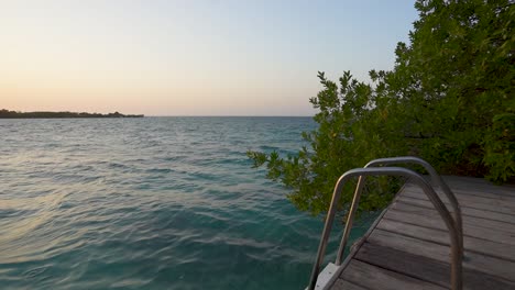 A-picturesque-scene-of-a-ladder-on-a-dock-extending-into-the-ocean,-against-stunning-sunset-over-ocean-waves