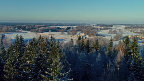 Amanecer-Aéreo-De-Invierno-Sobre-Bosques-Y-Campos-Cubiertos-De-Nieve,-Acogedor-Paisaje-Rural